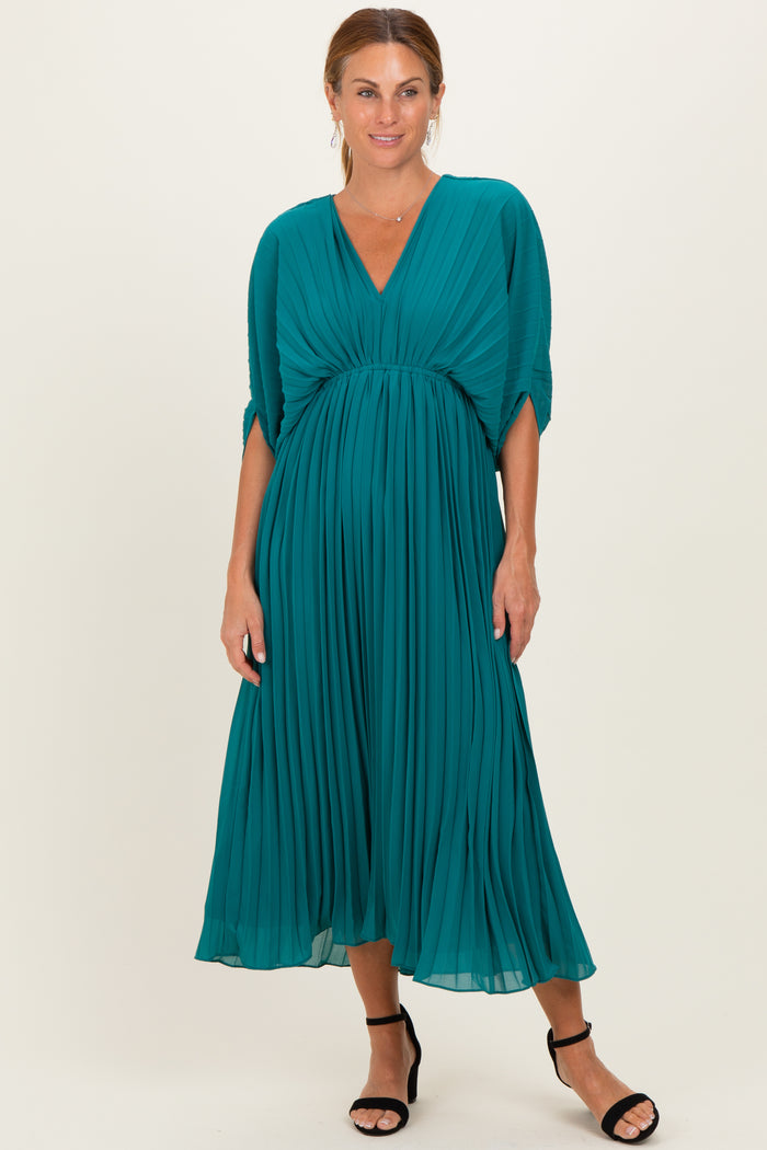woman wearing a teal pleated midi dress with a deep v-neck and short sleeves, styled with black heeled sandals