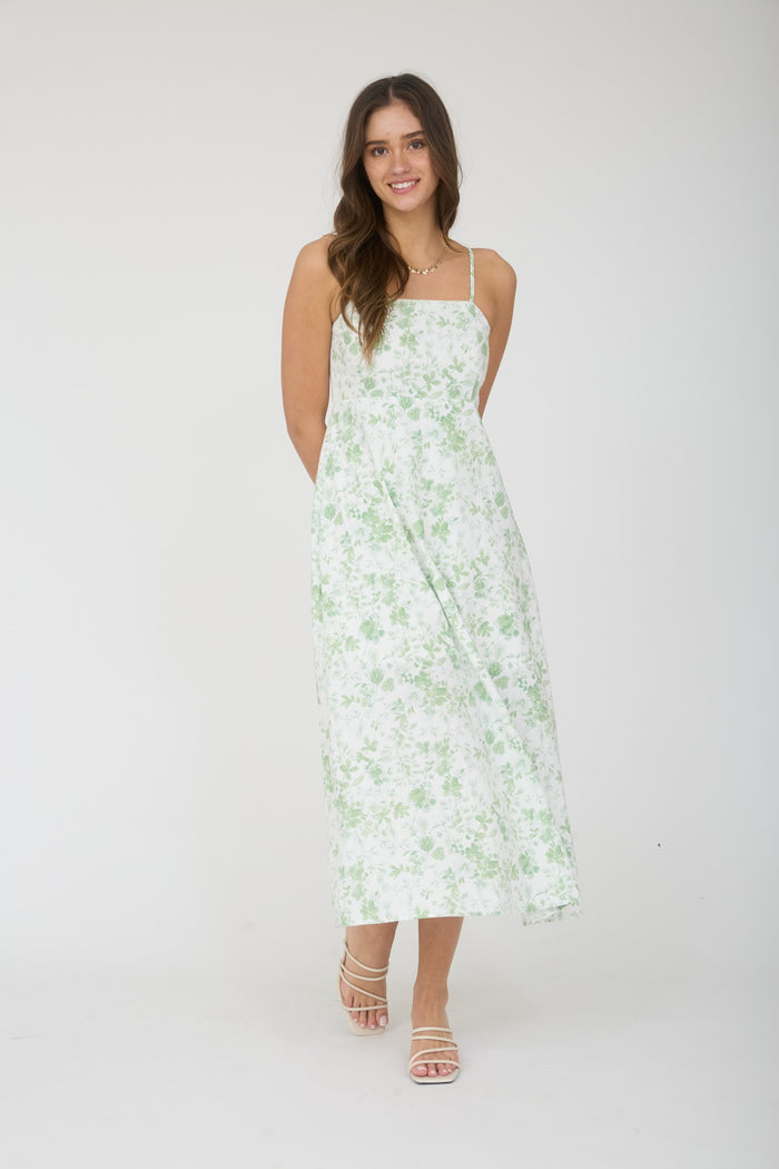 woman wearing a white maxi dress with green floral print and thin straps