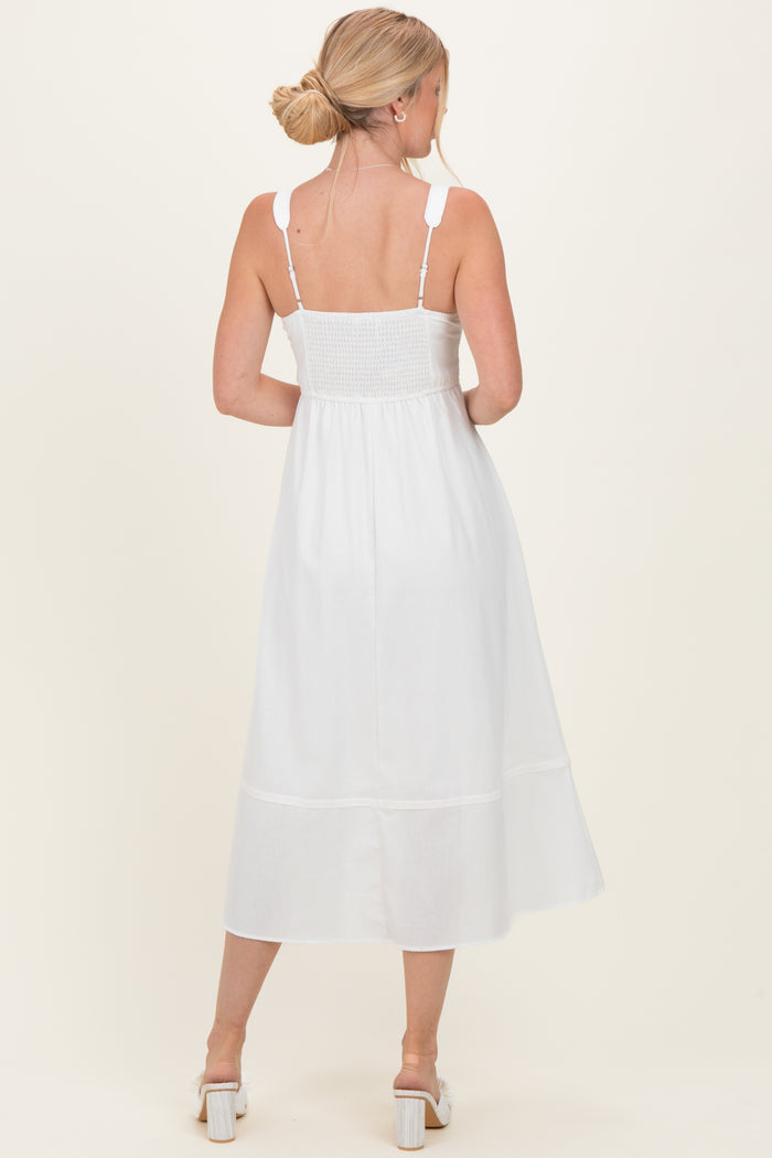 woman wearing a white mid-length sundress with smocked bodice and adjustable straps, shown from the back