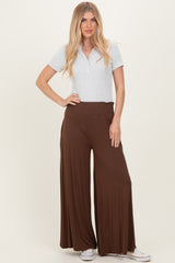 woman wearing a grey polo shirt and brown wide-leg pants, standing with one hand on her hip