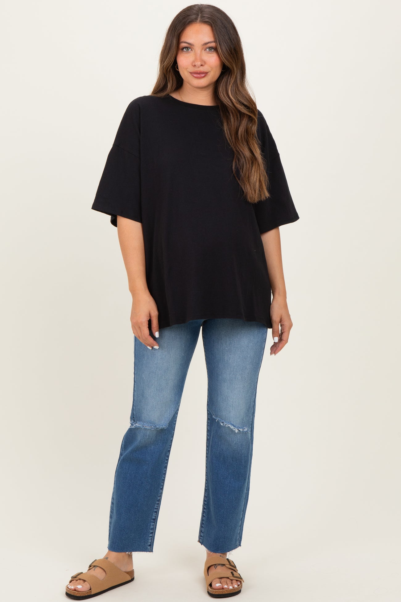 woman wearing a black oversized maternity t-shirt and distressed light blue jeans with a visible baby bump