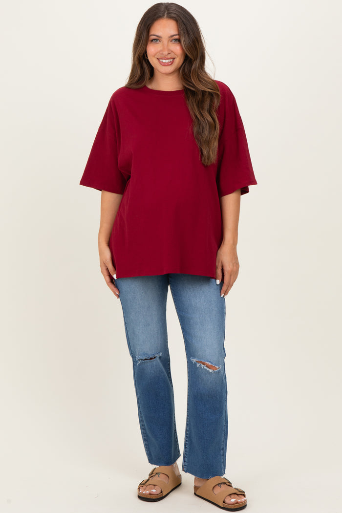 woman wearing a burgundy oversized maternity top and distressed blue jeans