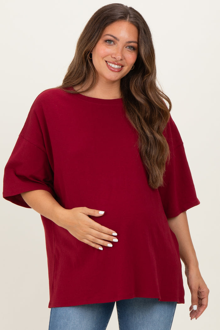 woman wearing a burgundy oversized maternity top and holding her baby bump