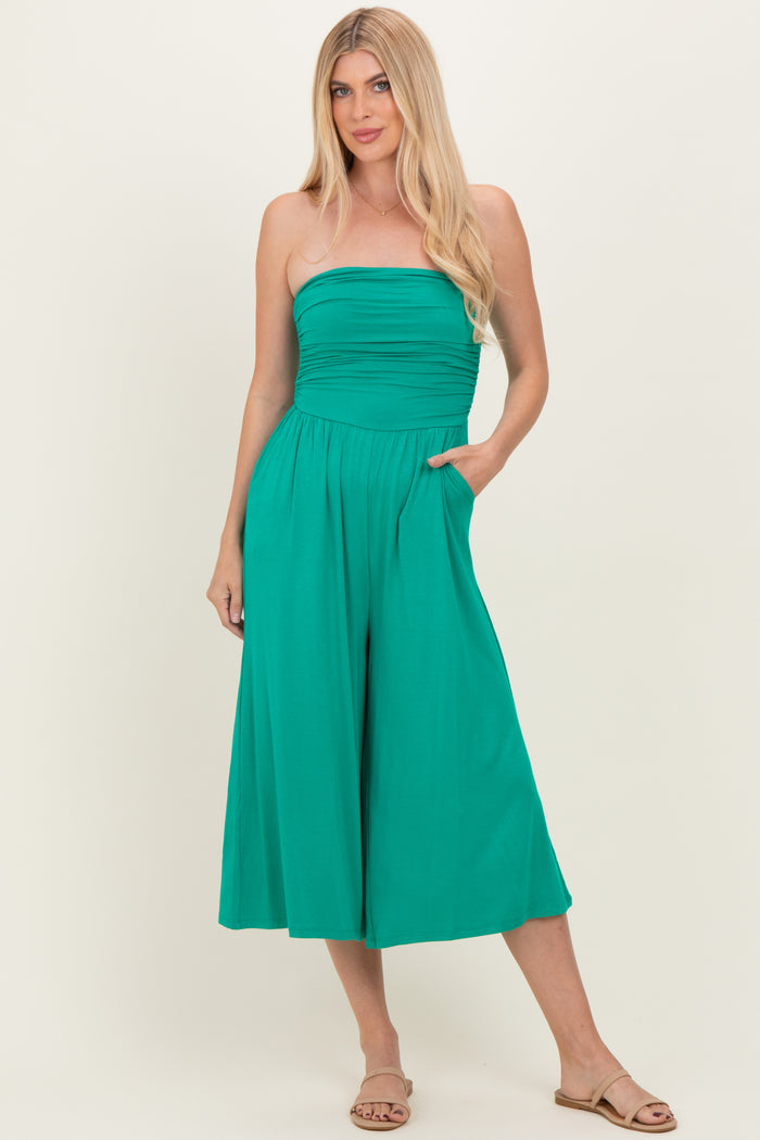 woman wearing a strapless teal jumpsuit with a ruched bodice and wide legs, posing with hands in pockets
