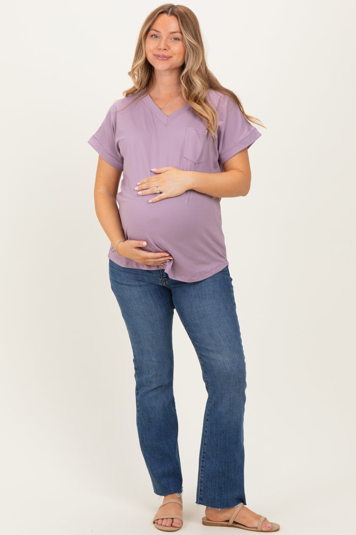 woman wearing a lilac maternity top with a pocket and denim flared jeans, holding her baby bump