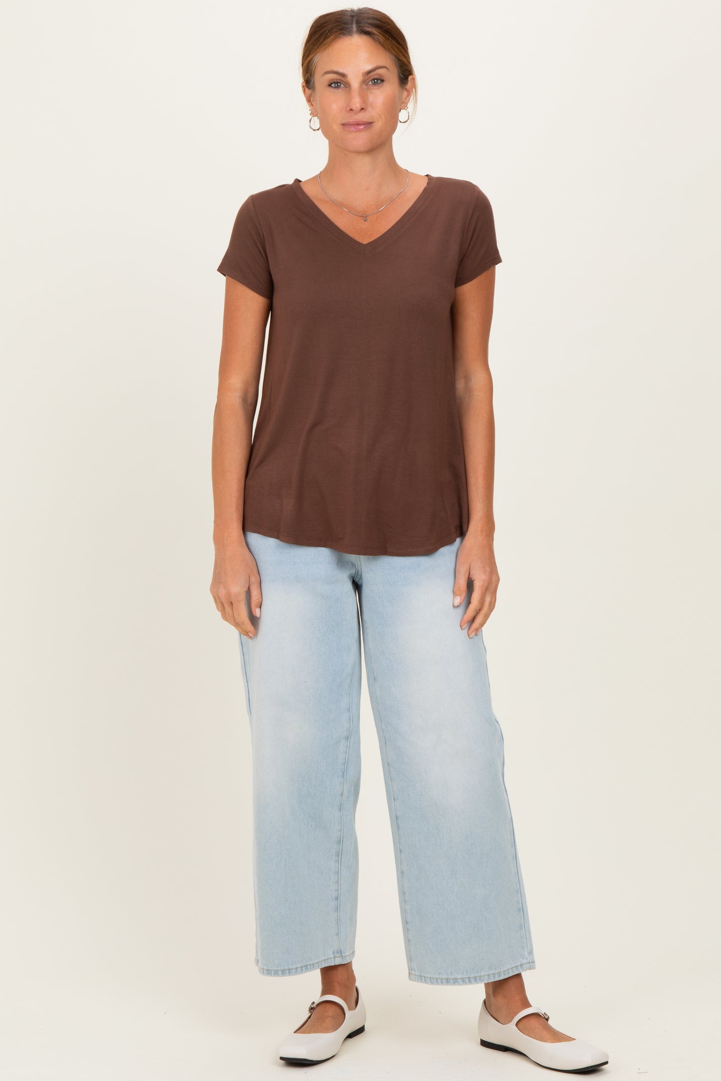 woman wearing a brown v-neck short sleeve t-shirt and light blue wide-leg jeans, standing in a neutral background