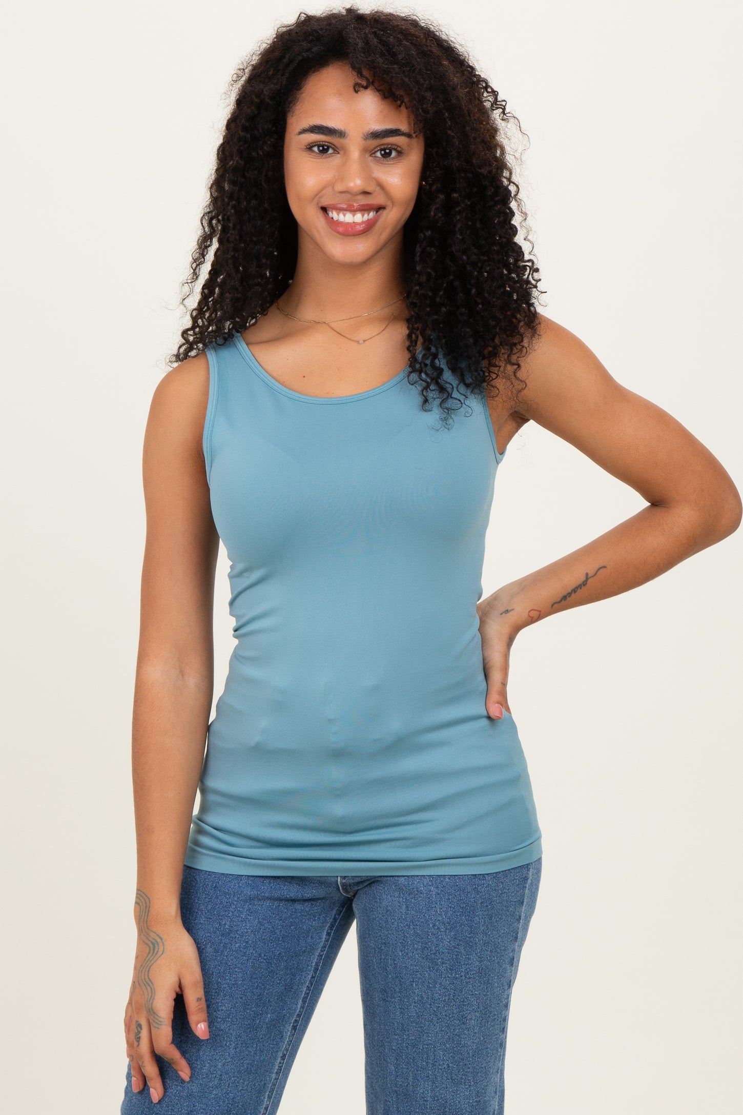 woman wearing a light blue form-fitting tank top and blue high-waisted jeans, smiling at the camera