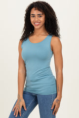woman wearing a light blue fitted tank top and blue high-waisted jeans, smiling at the camera