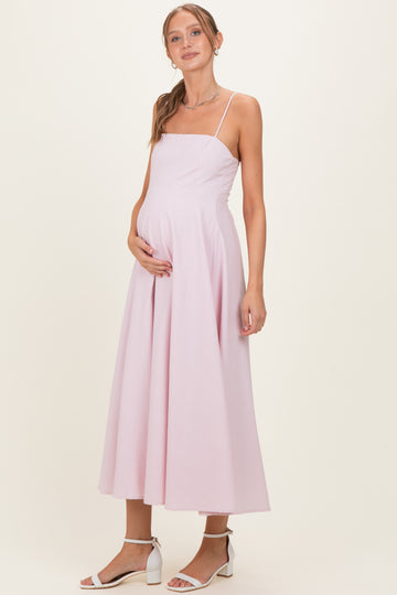 woman wearing a light pink maternity gown with a fitted bodice and flowing skirt, holding her baby bump