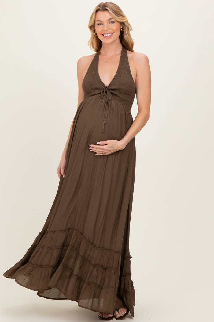 woman wearing a brown maternity maxi dress with a halter neck and ruffle details, gently cradling her baby bump