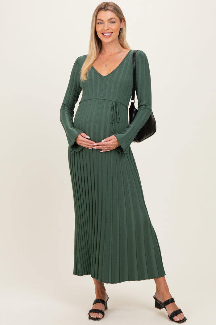 woman wearing a green long sleeve maternity dress with pleats, holding her baby bump