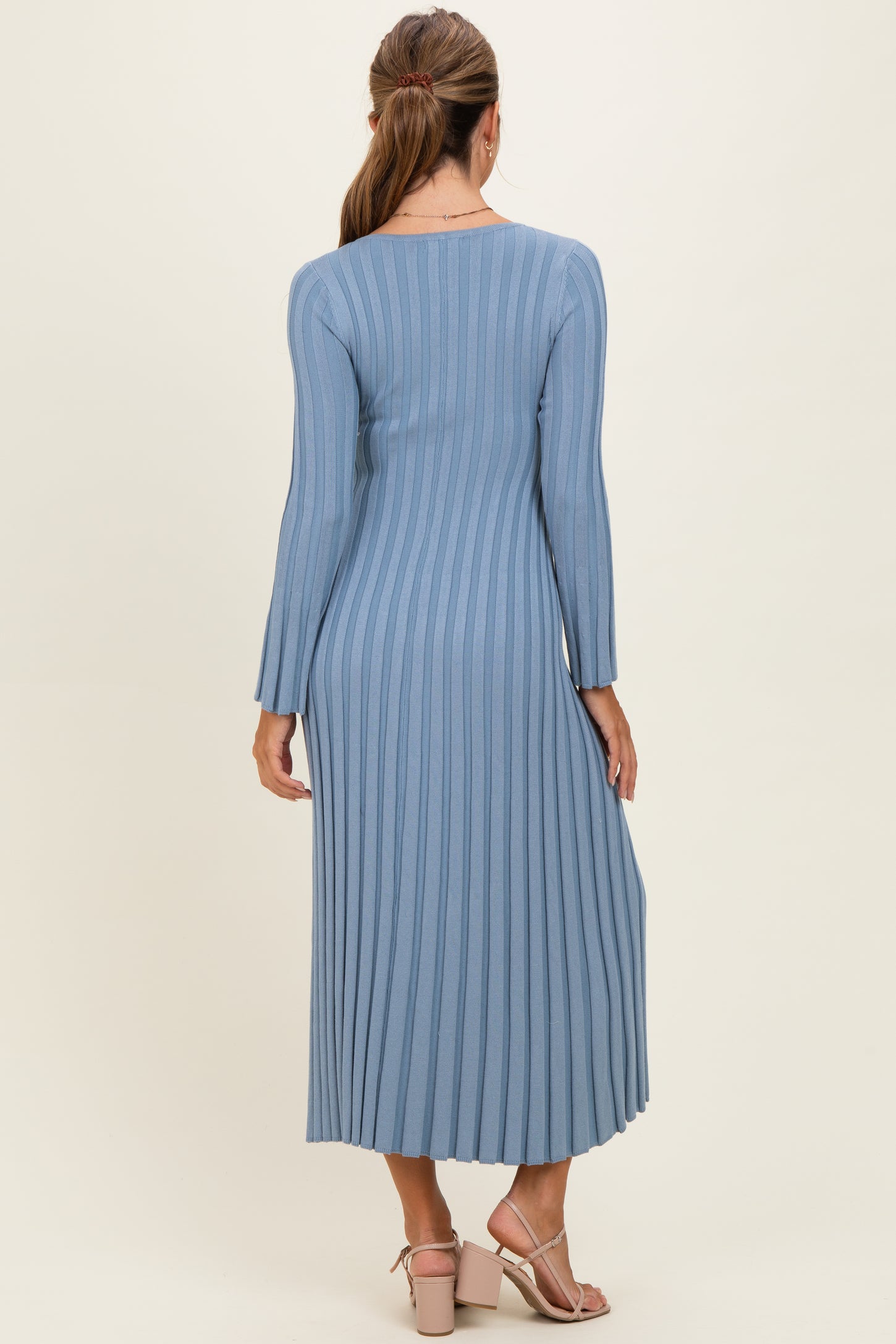 woman wearing a long sleeve ribbed midi dress in light blue, showing the back view with a fitted silhouette and side pleats