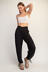 woman wearing a white crop top and black drawstring jogger pants, smiling and posing with one hand on her hip