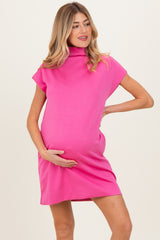 woman wearing a bright pink maternity dress with a high neckline and short sleeves, holding her baby bump