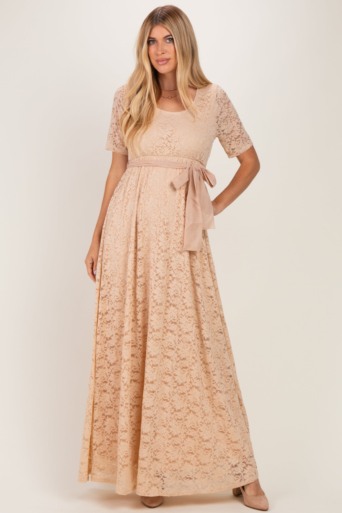 woman wearing a beige lace maxi dress with short sleeves and a tied waist sash