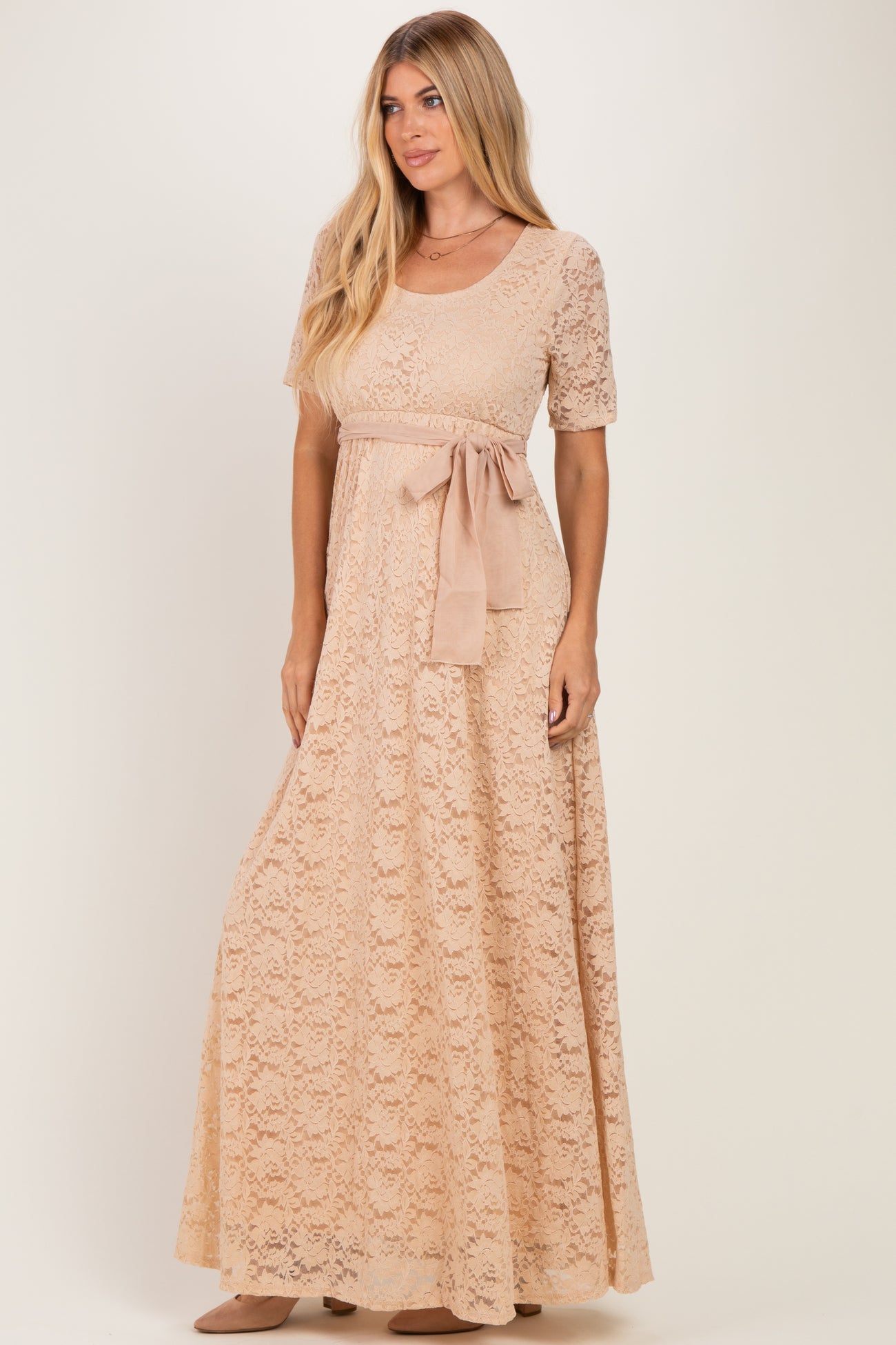 woman wearing a blush lace maxi dress with short sleeves and a ribbon belt tied at the waist