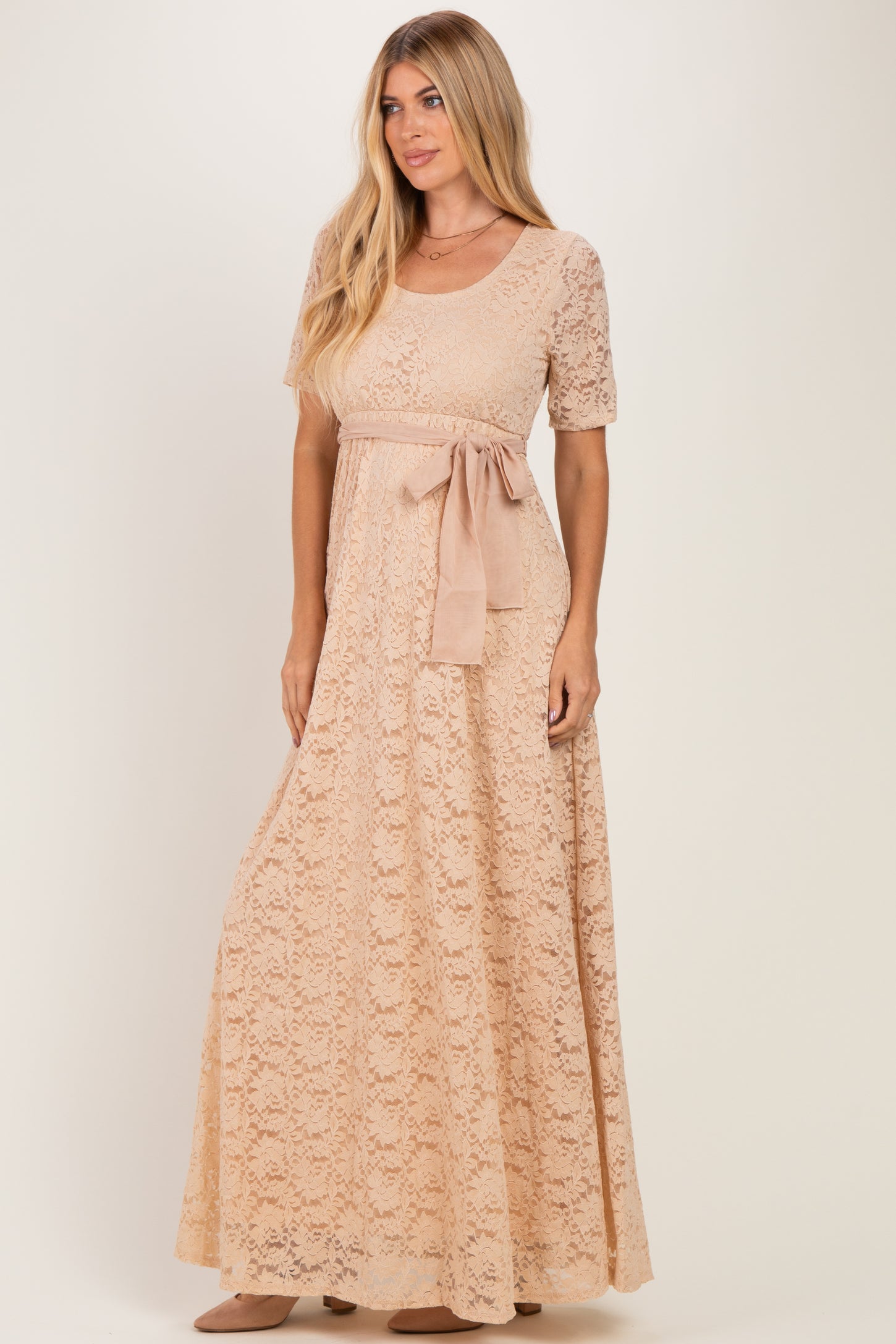 woman wearing a blush lace maxi dress with short sleeves and a ribbon belt tied at the waist