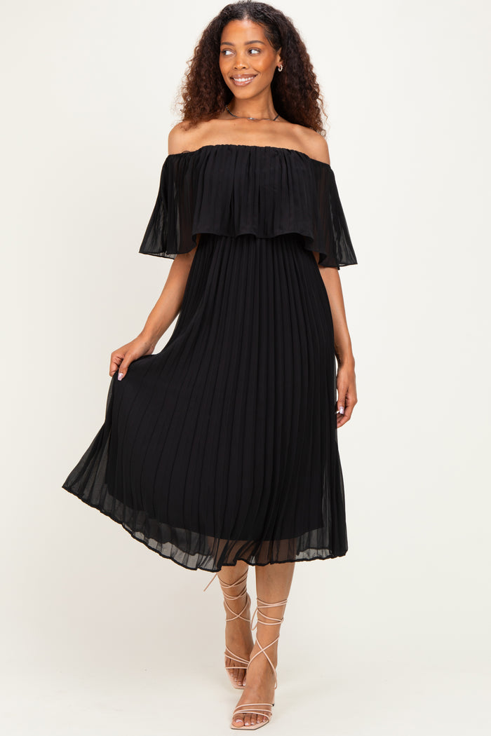 woman wearing a black off-shoulder pleated midi dress with ruffle details and strappy sandals