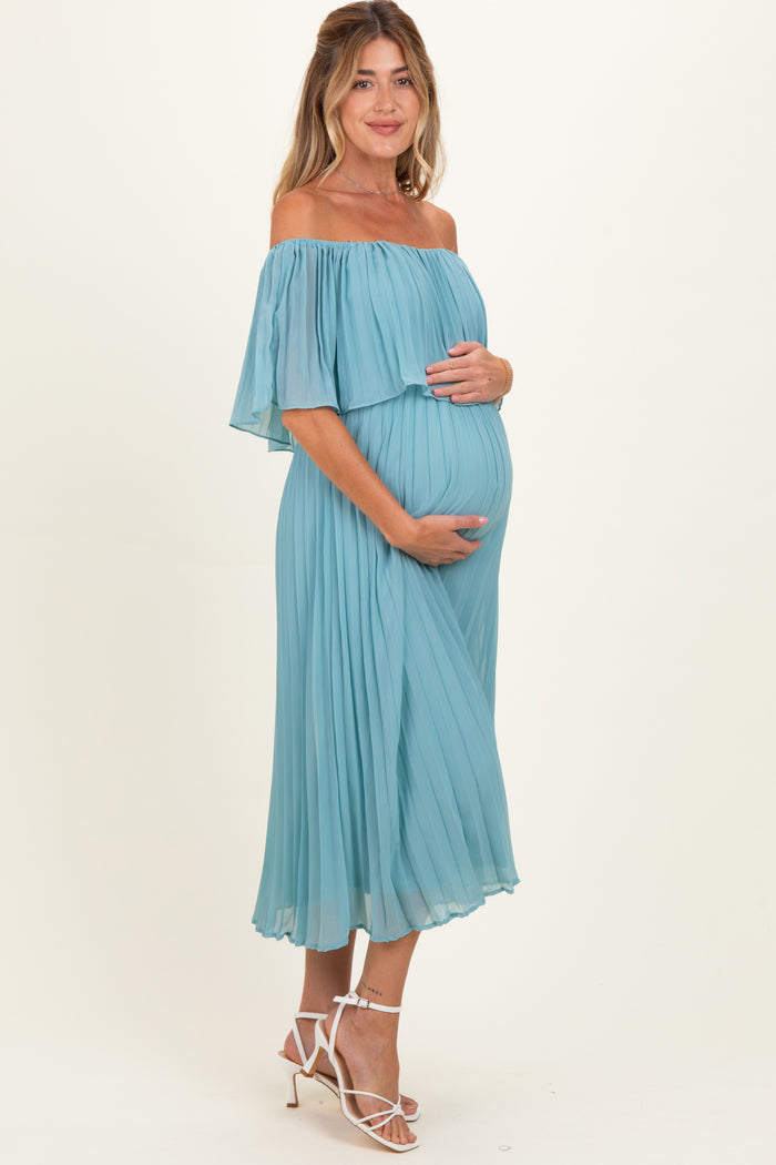 woman wearing a light blue off-the-shoulder maternity dress and holding her baby bump