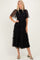 woman wearing a black tiered midi dress with sheer short sleeves and a smocked bodice, paired with green heels