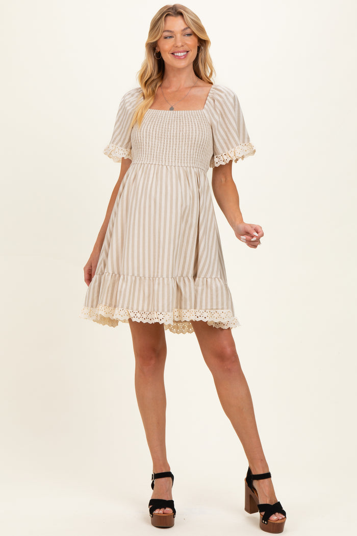 woman wearing a beige striped maternity dress with short sleeves and lace trim, smiling and posing