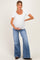 woman wearing a white short sleeve maternity top and blue flared jeans, cradling her baby bump