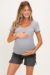 woman wearing a gray striped maternity top and black shorts, holding her baby bump