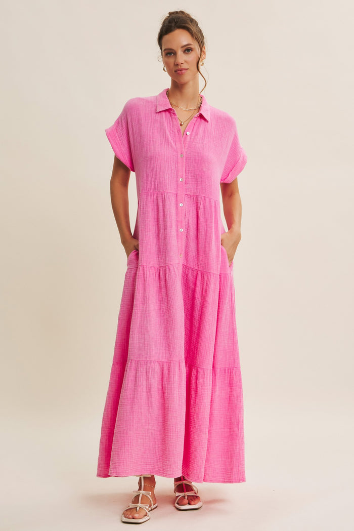 woman wearing a pink button-up maxi dress with short sleeves and pockets, standing against a neutral background
