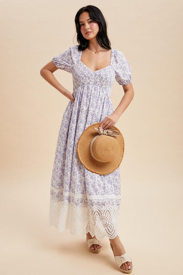 woman wearing a lavender floral maxi dress with puff sleeves and lace trim, holding a straw hat