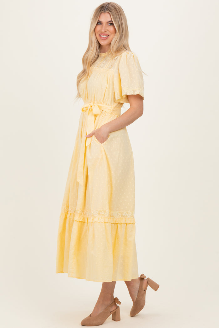 woman wearing a yellow midi dress with puff sleeves, a tie waist, and ruffle hem, styled with embellished heels