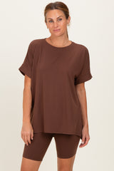 woman wearing a brown oversized t-shirt and matching bicycle shorts, standing against a neutral background