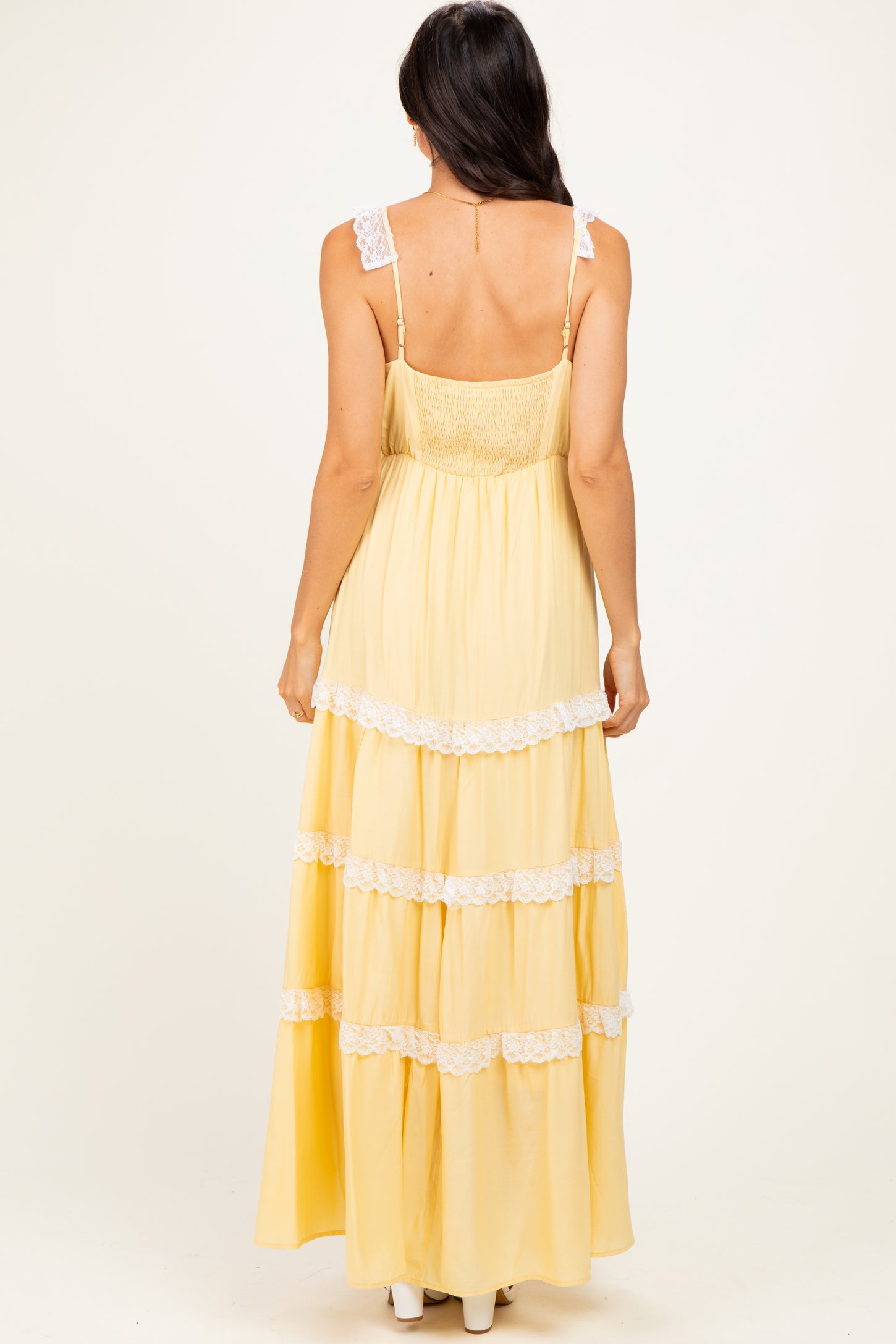 woman wearing a yellow maxi dress with lace trim and a smocked bodice, shown from the back