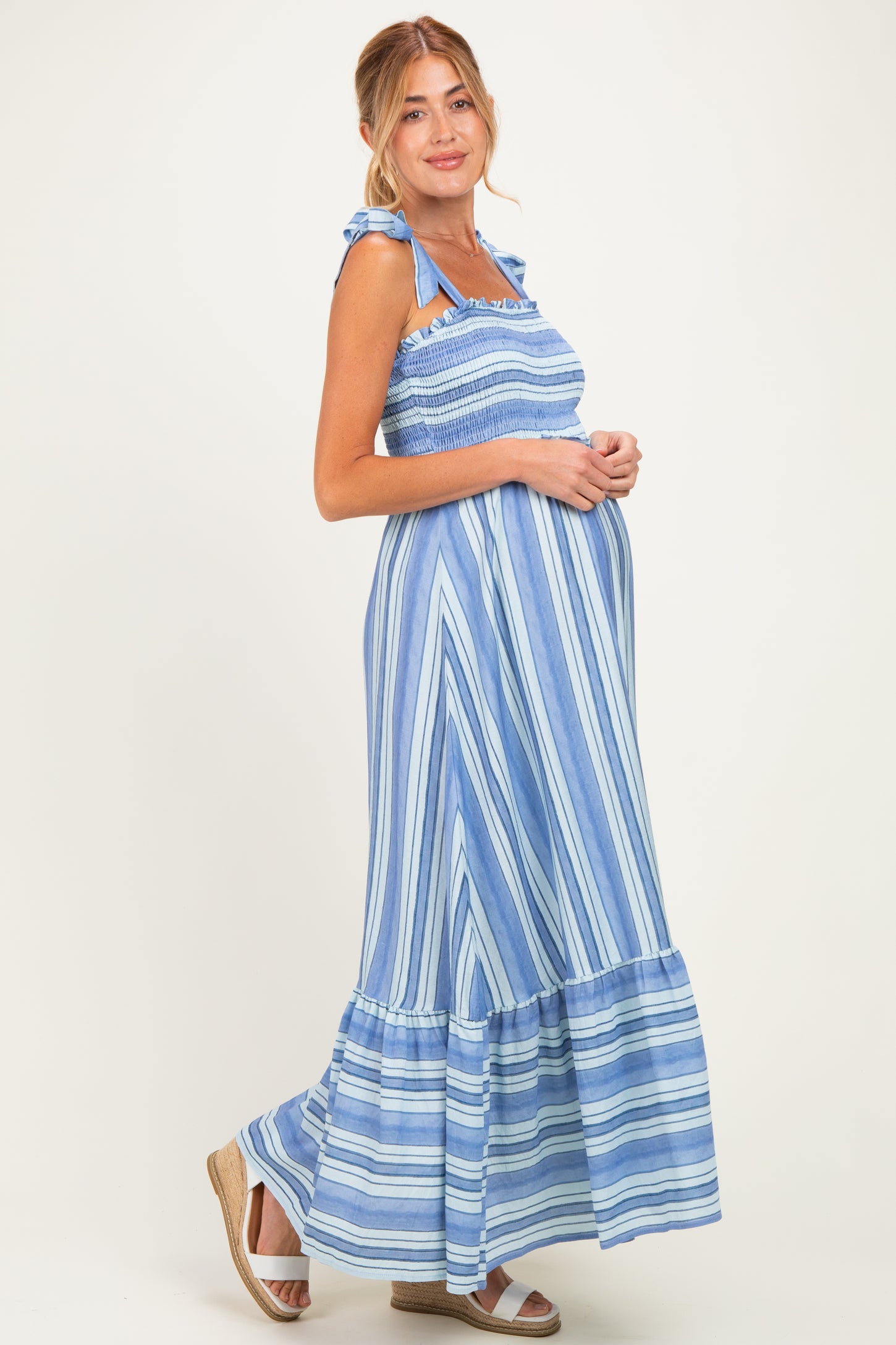 woman wearing a blue and white striped maternity maxi dress, carrying a baby bump, with tied straps and a tiered hem