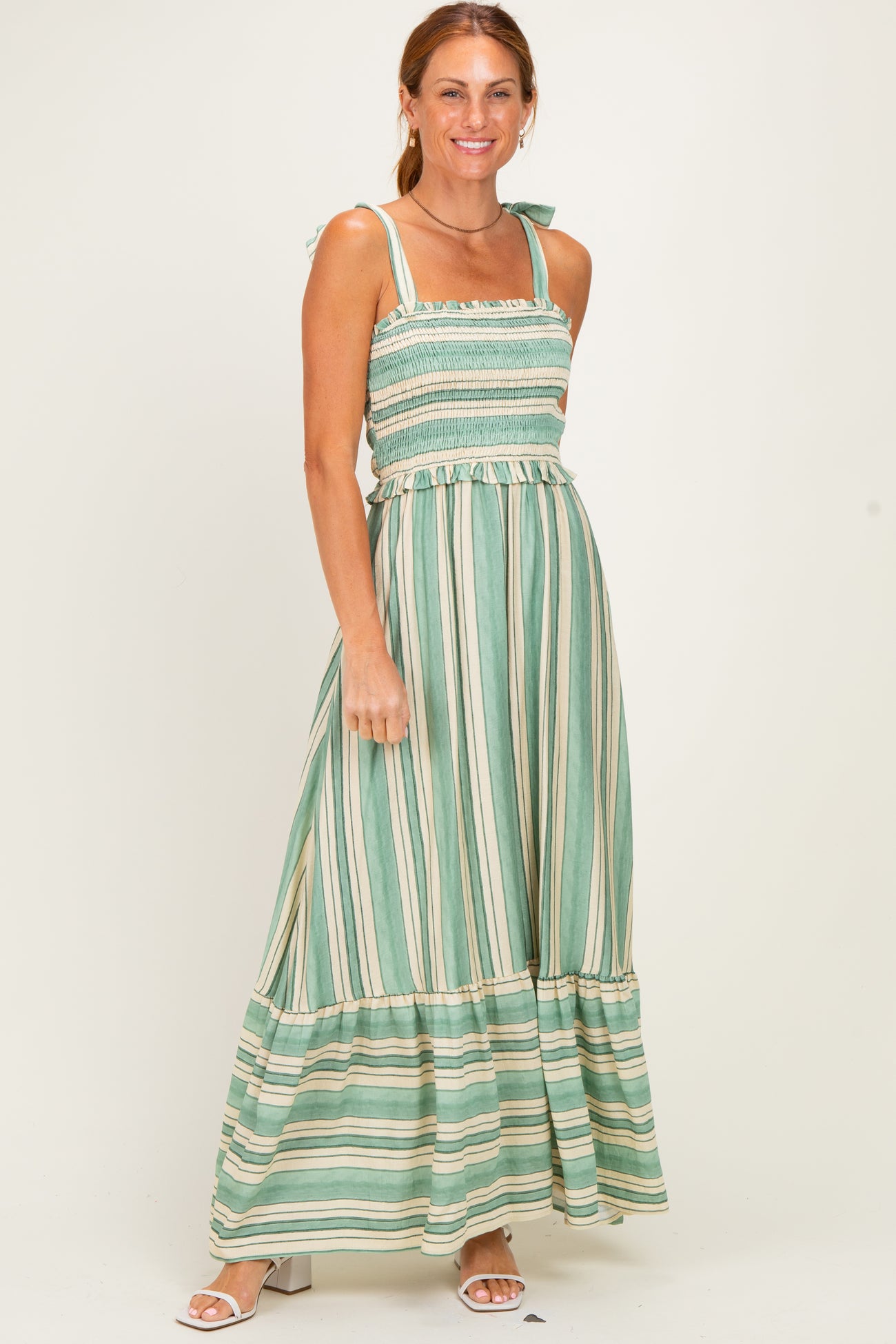 woman wearing a green striped maxi dress with smocked bodice and tie straps, standing and smiling