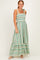woman wearing a green striped maxi dress with smocked bodice and tie straps, standing and smiling