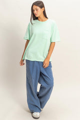 woman wearing a mint green oversized t-shirt with a pocket and blue baggy jeans standing against a neutral background