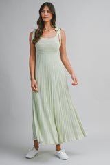 woman wearing a light green maxi dress with smocked bodice and tie straps, paired with white sneakers