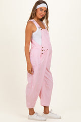 woman wearing a pink striped maternity overalls with a white tank top and a headband, showing her baby bump
