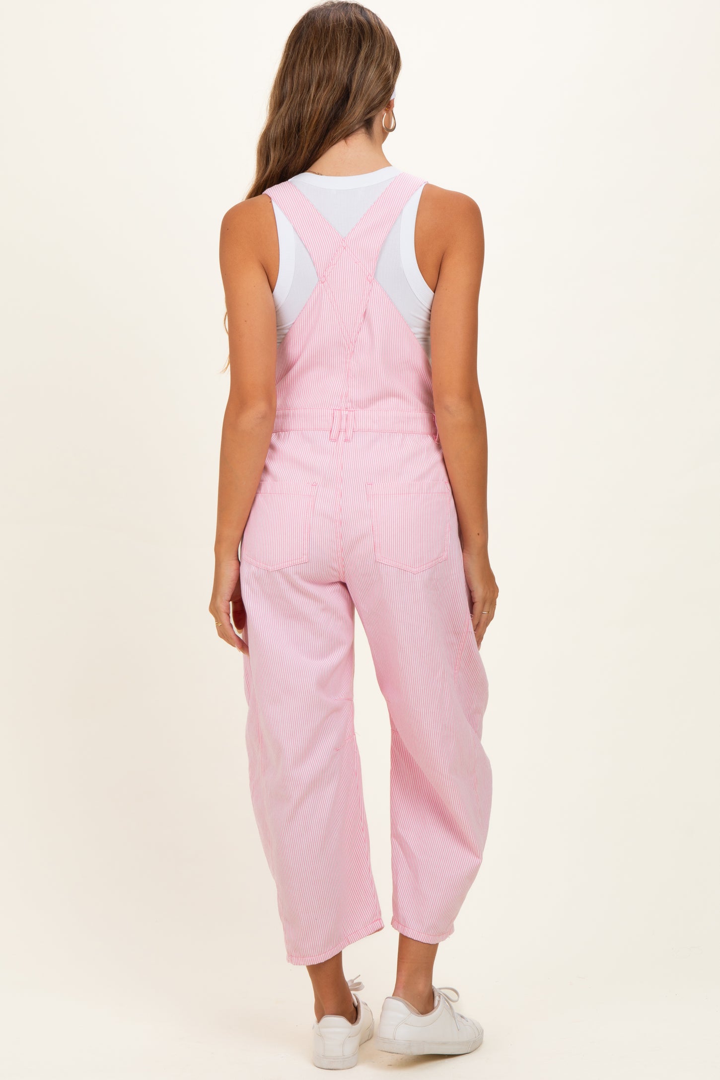 woman wearing pink striped maternity overalls with a loose fit and a white tank top underneath, showing the back view