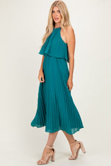woman wearing a teal pleated midi dress with a layered halter top and nude high-heeled sandals
