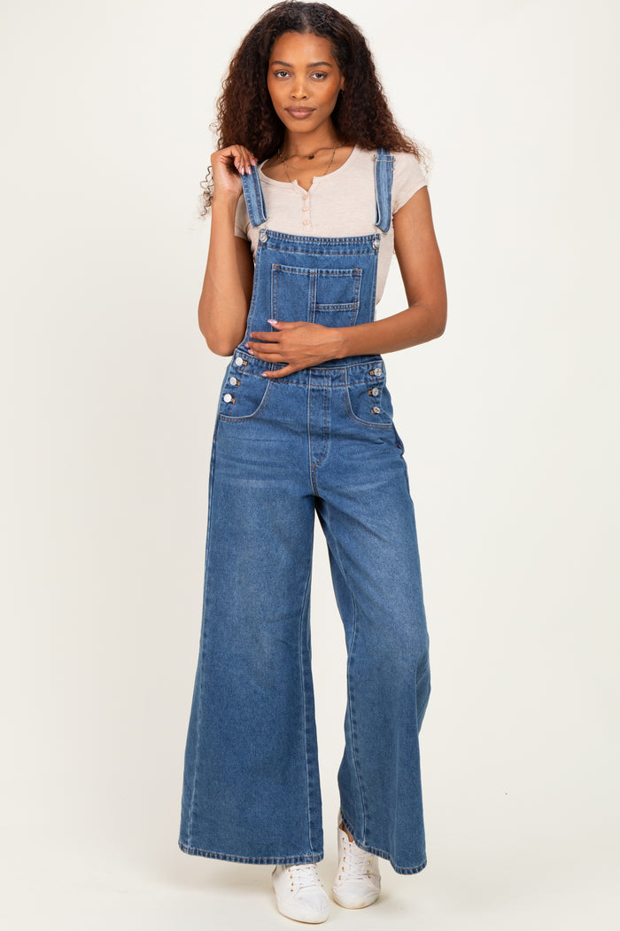 woman wearing a light gray short sleeve top with blue wide-leg denim overalls and white sneakers