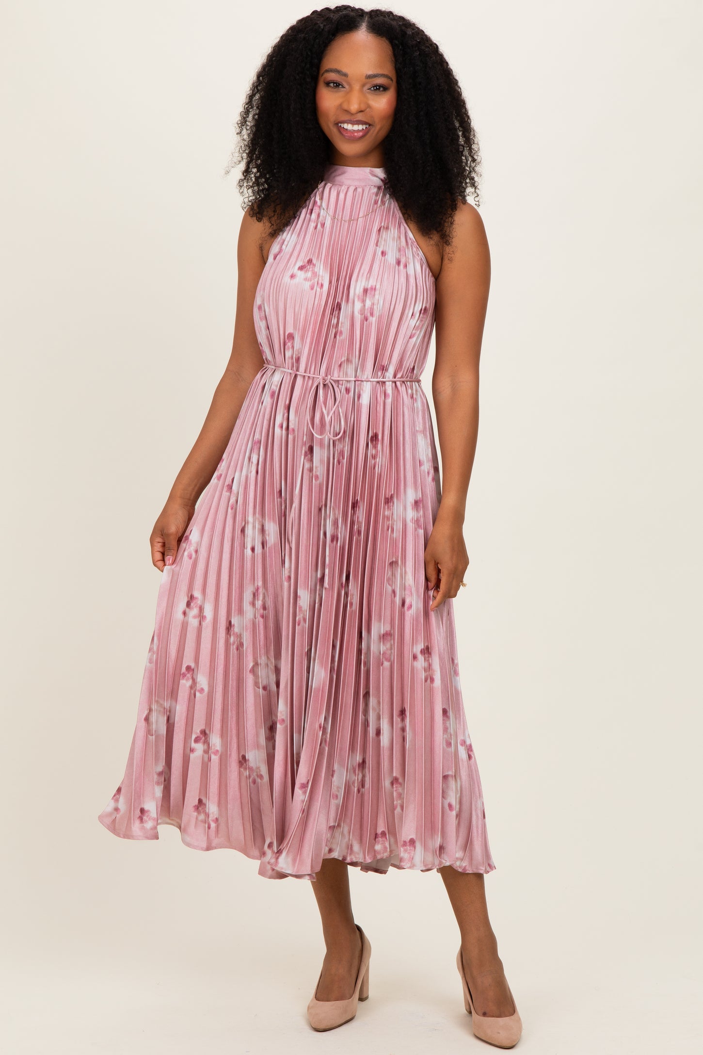 woman wearing a pink floral pleated midi dress with a halter neck and cinched waist