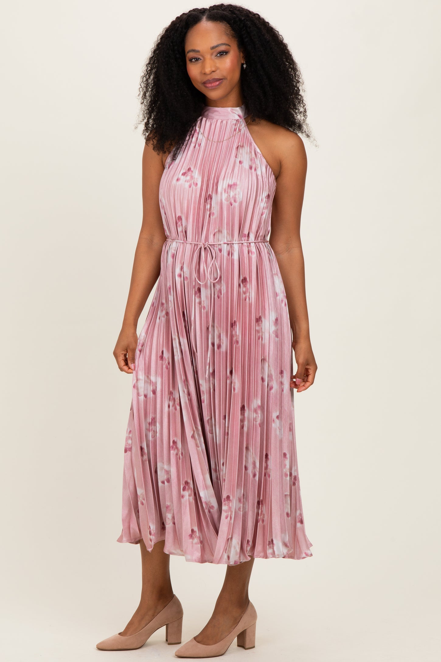woman wearing a pink floral pleated halter dress with a tie waist and knee-length skirt