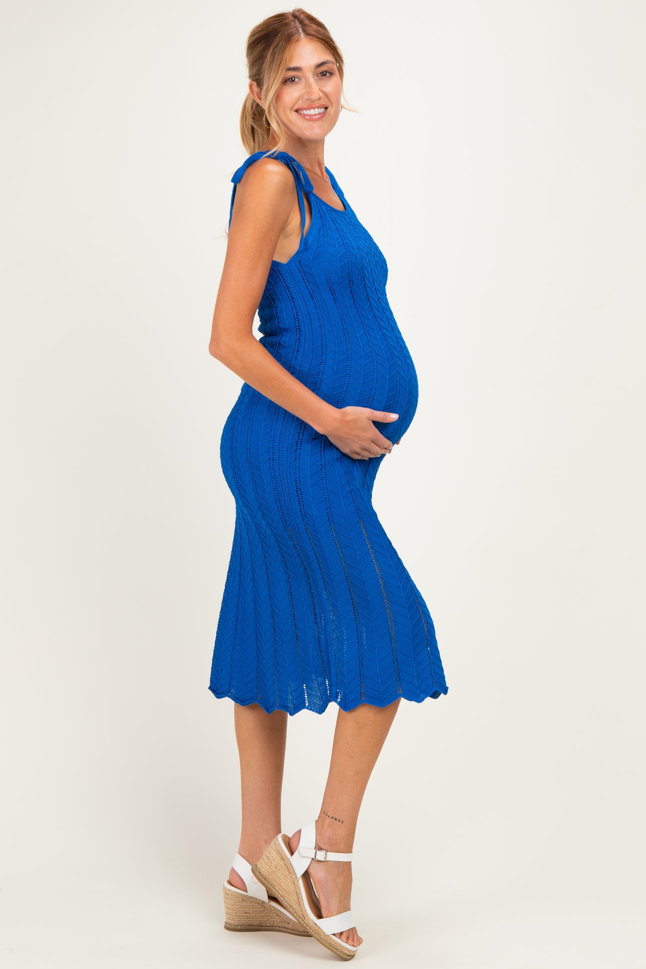 woman wearing a vibrant blue maternity midi dress with tie straps and a visible baby bump, standing sideways