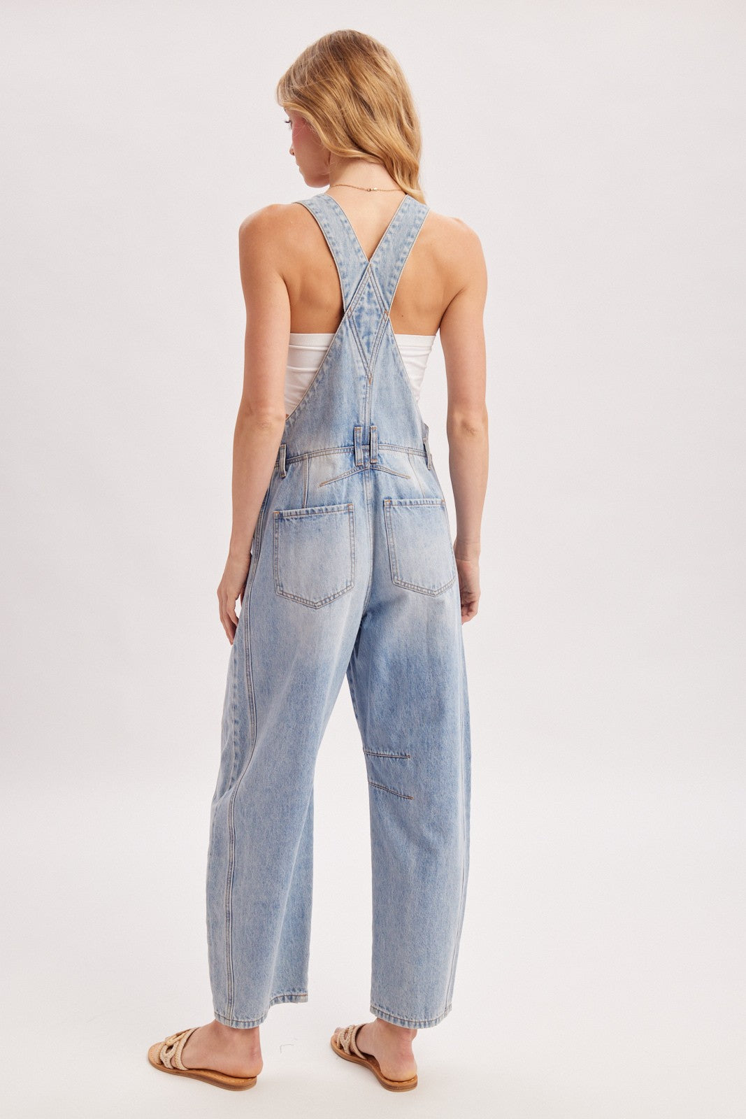 woman wearing light blue denim overalls with a loose fit and adjustable straps, seen from the back