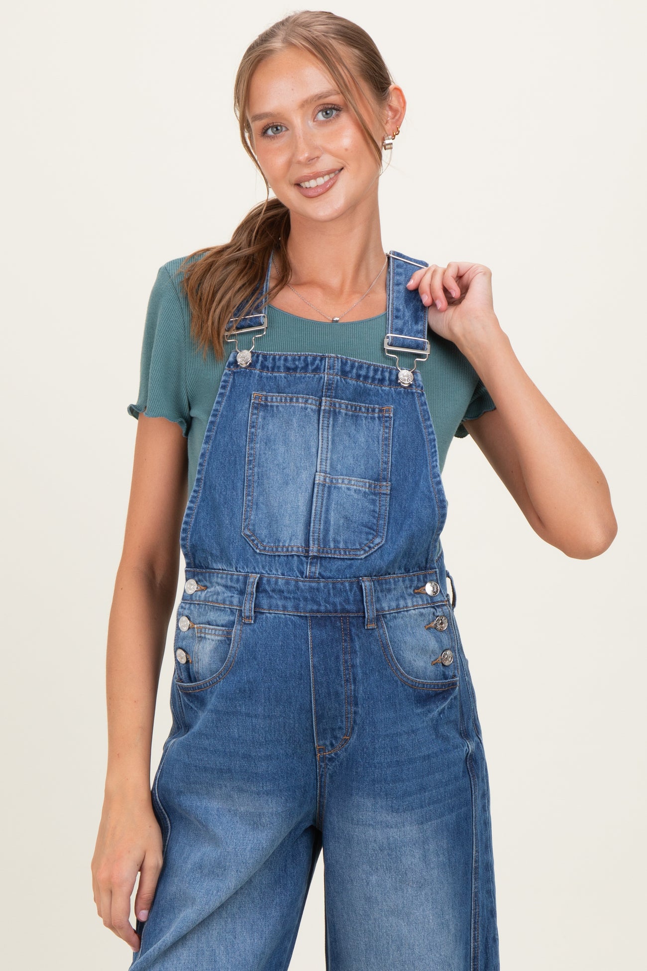 woman wearing a green short sleeve top under blue denim maternity overalls with adjustable straps