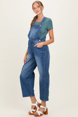 woman wearing a blue maternity overall with a green top and standing in a side pose