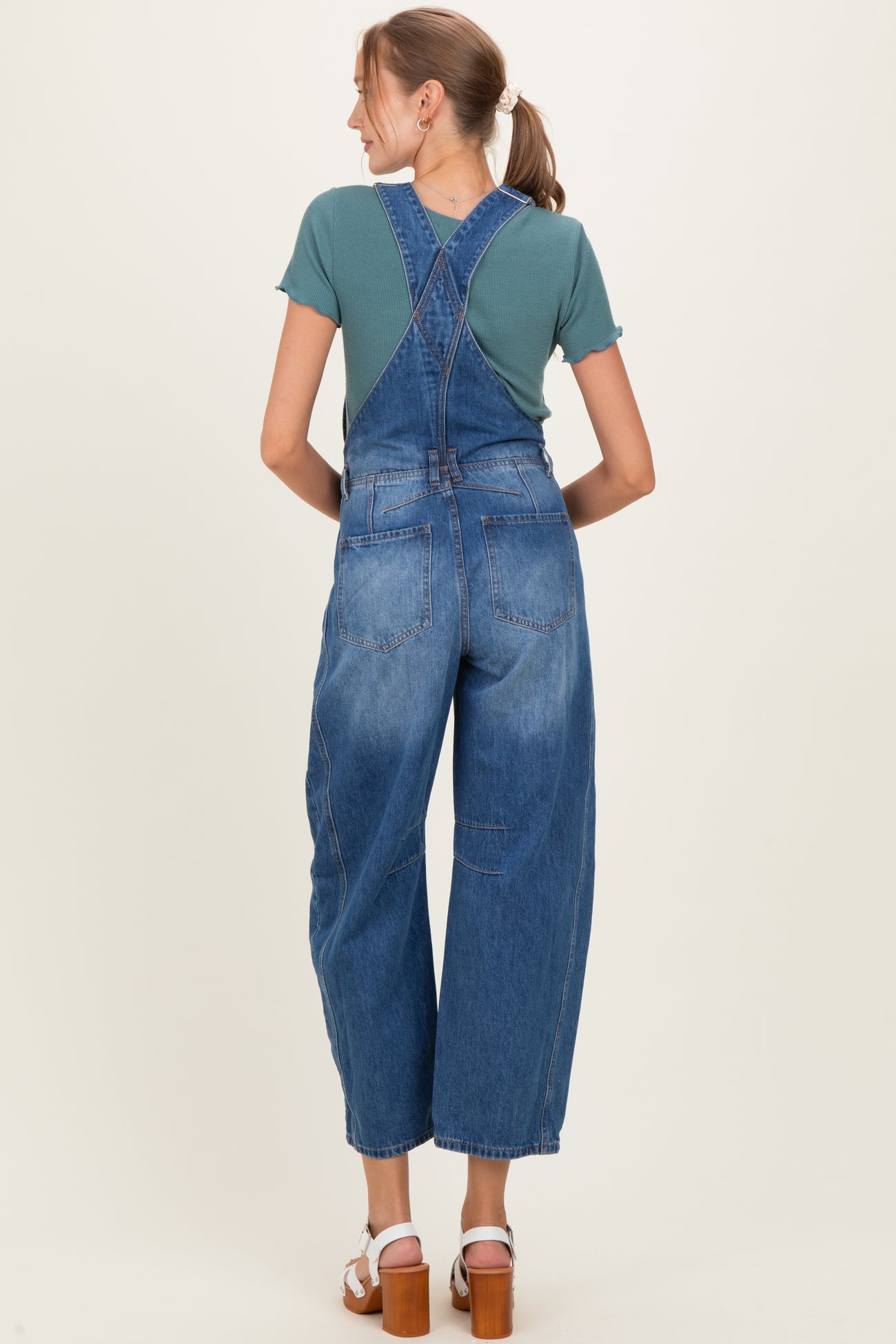 woman wearing a teal short sleeve top and blue maternity overalls, viewed from the back
