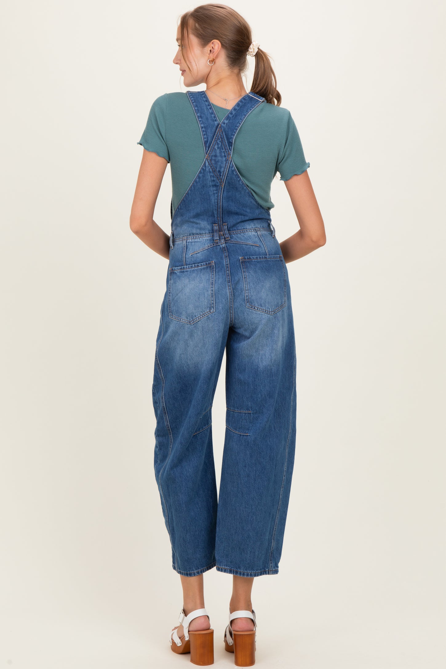 woman wearing a teal short sleeve top and blue maternity overalls, viewed from the back
