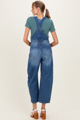 woman wearing a teal short sleeve top and blue maternity overalls, viewed from the back